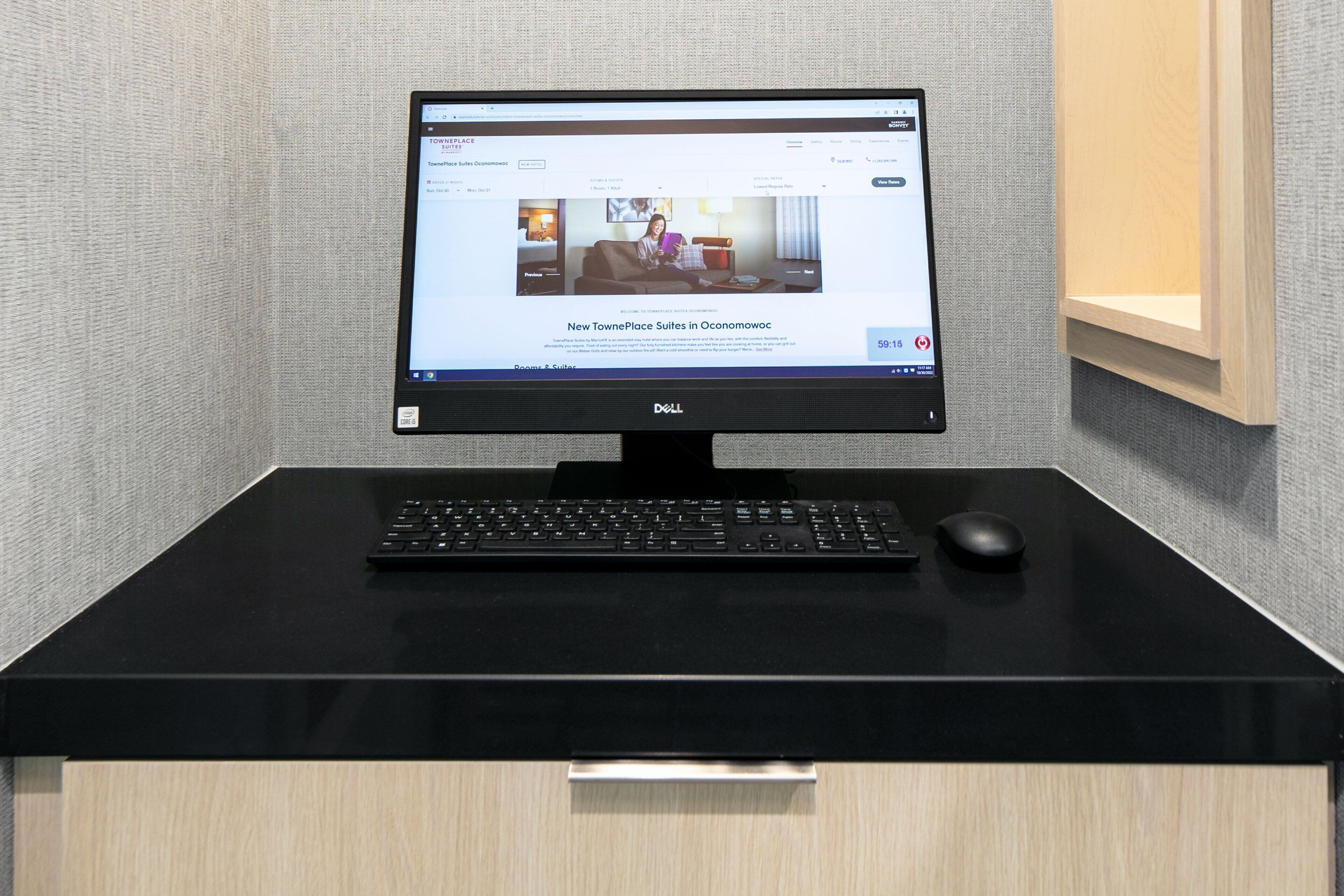 A Dell monitor on a black desk with a keyboard and mouse, displaying a webpage about TownePlace Suites in Oconomowoc.