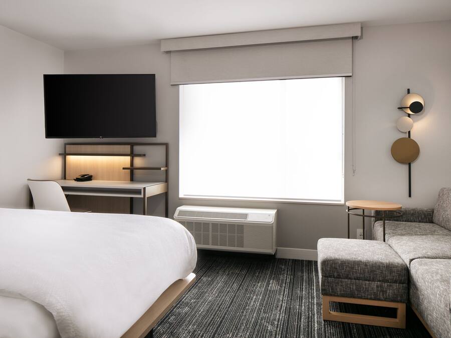 Et moderne hotelværelse med en stor seng, et skrivebord med et fladskærms-tv, et lille bord og en sofa.