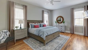 A bedroom with a bed, a nightstand, a dresser, a ceiling fan, and a window with curtains.