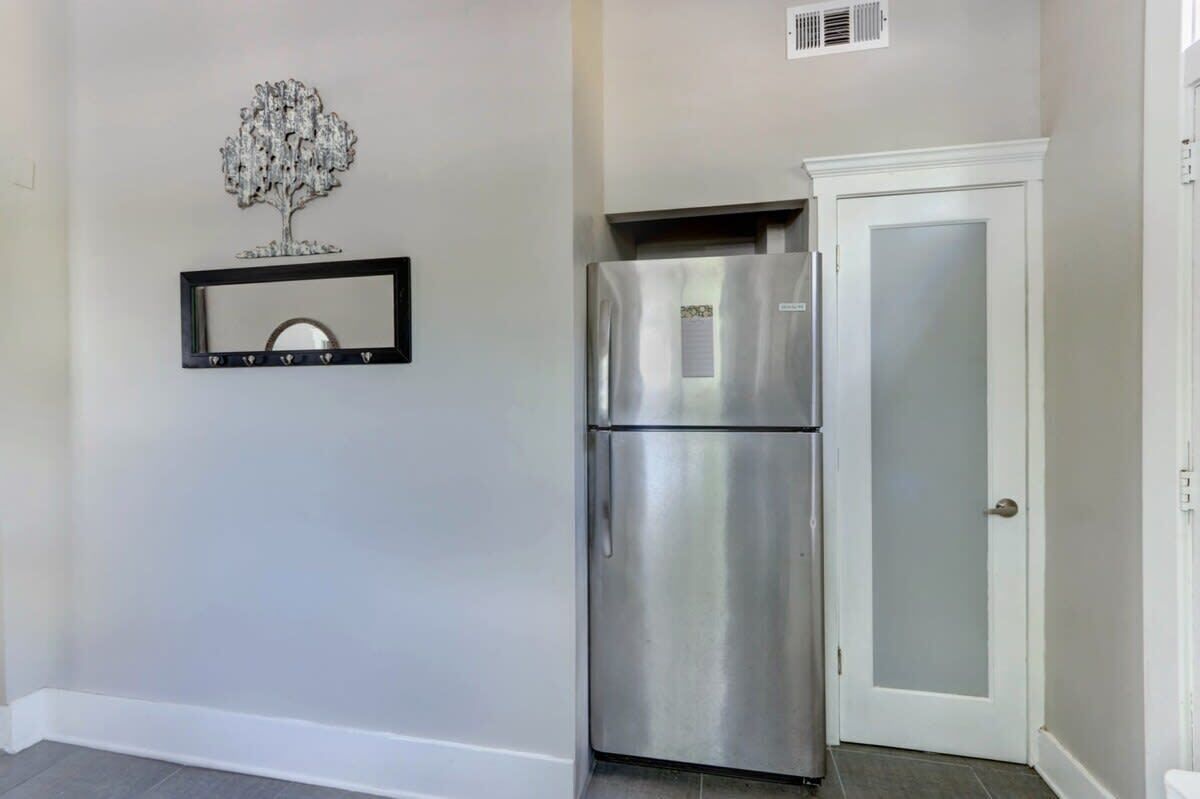A kitchen with a stainless steel refrigerator, a white cabinet, and a decorative tree on the wall.