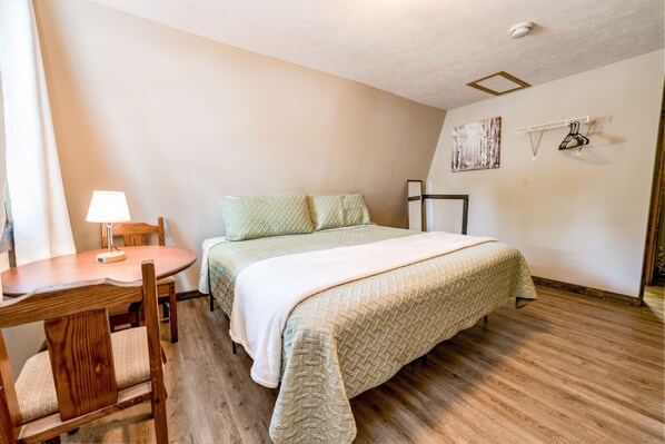 Cozy retreat with a single bed, nightstand, and chair, set against a light-colored wall and wooden floor.