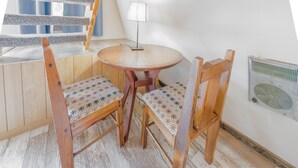 Un rincón acogedor con una mesa redonda de madera, dos sillas de madera con cojines estampados, una lámpara pequeña y un radiador en la pared.
