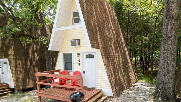 Een chalet met een schuin dak, een klein terras met rode Adirondack stoelen en een zwarte barbecue.