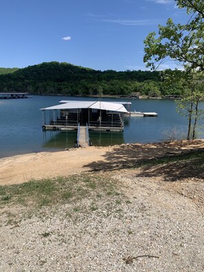 A docked boat with a covered seating area and a small pier extending into a lake. - A-Frame Cabin on Table Rock Lake- by SDC! (Branson)