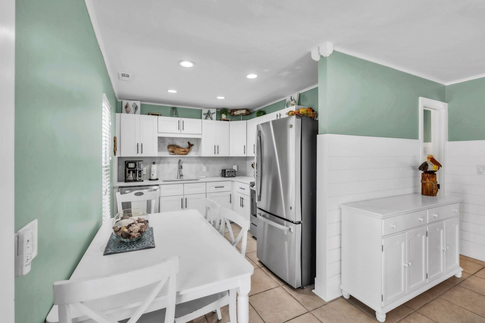 A compact kitchen with white cabinets, a stainless steel refrigerator, and a dining table with chairs.
