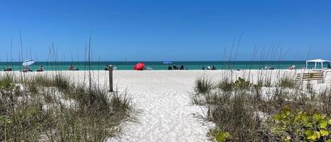 A sandy beach path leading to the ocean with beach umbrellas and a white canopy.
