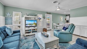 Una sala de estar con una televisión, un mueble blanco para entretenimiento y un sofá color turquesa.