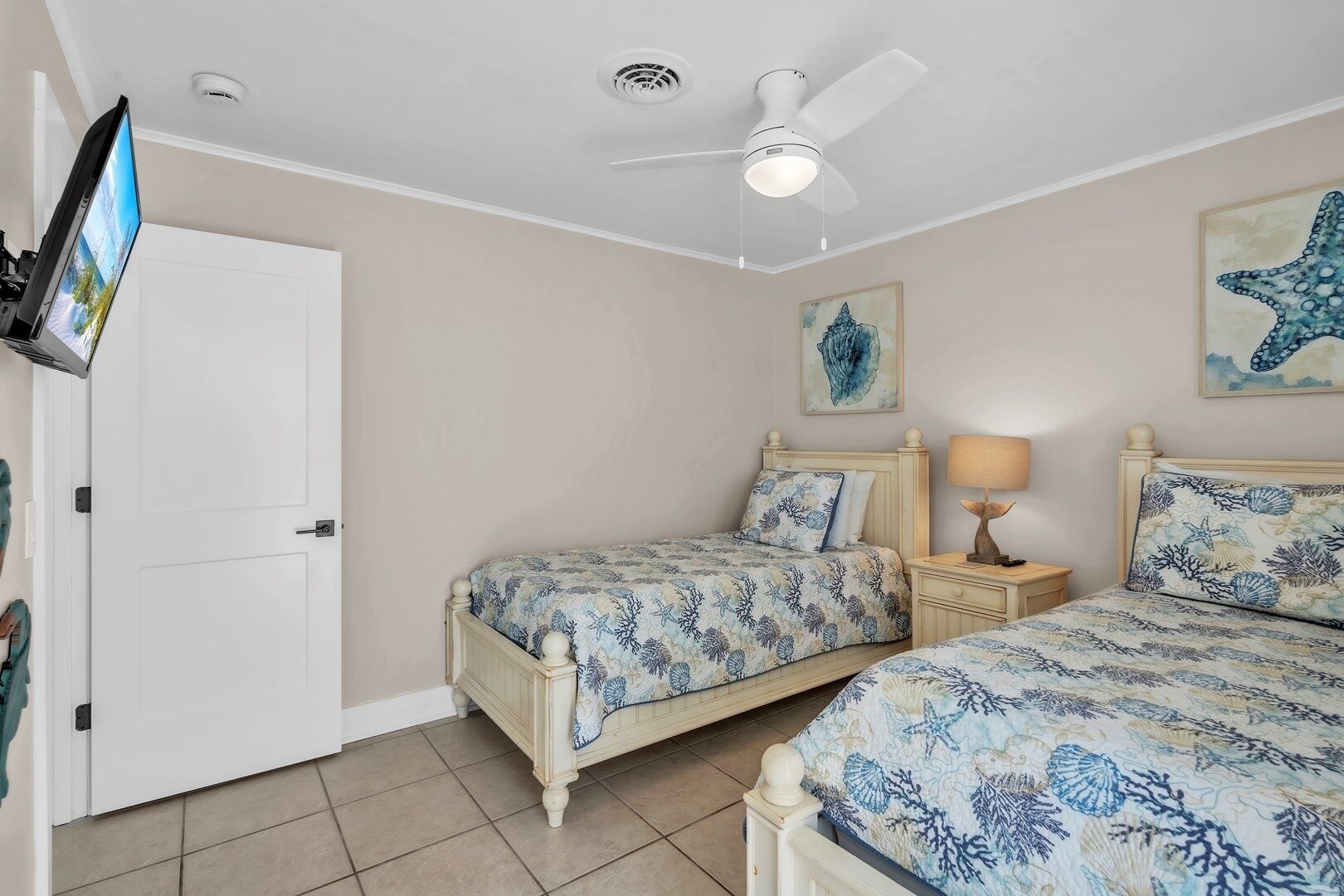 A bedroom with two beds, a ceiling fan, a TV, and artwork on the walls.