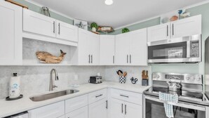 Una cocina moderna con armarios blancos, un lavamanos de acero inoxidable, un microondas y un horno.