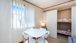 A room with a white table and chairs, a window with blinds, a lamp, and a bunk bed with floral bedding. - Getaway to Cabin 49- this charming, cute cabin located in the Geographe Holiday Park (Broadwater)