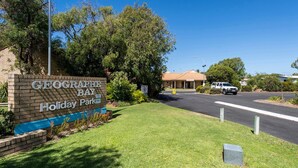 A sign for Geographe Bay Holiday Park with a clear road, a building in the background, and a parked car. - Getaway to Cabin 49- this charming, cute cabin located in the Geographe Holiday Park (Broadwater)