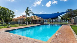 A rectangular swimming pool with a brick border, surrounded by a grassy area and a shaded structure. - Getaway to Cabin 49- this charming, cute cabin located in the Geographe Holiday Park (Broadwater)