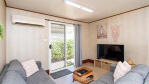A living room with two grey sofas, a flat-screen TV, a wicker coffee table, and a sliding glass door leading to a balcony. - Getaway to Cabin 49- this charming, cute cabin located in the Geographe Holiday Park (Broadwater)