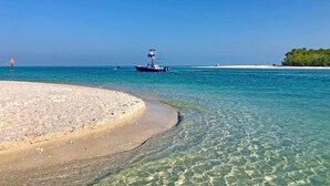 A beach with clear turquoise water, a boat, and a small island with trees. - Romantic vacation spot by the water with private heated pool and spa, kayaks! (Cape Coral)