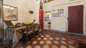 A room with a wooden ceiling, a chandelier, a table with a patterned tablecloth, a red curtain, and a hexagonal tiled floor. - Pinocchio by Mmega (Florence)