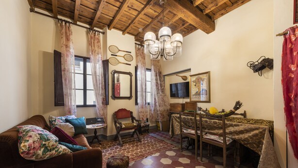 A living room with a brown sofa, a wooden dining table with a patterned tablecloth, and a chandelier. - Pinocchio by Mmega (Florence)