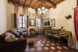 A living room with a brown sofa, a wooden dining table with a patterned tablecloth, and a chandelier. - Pinocchio by Mmega (Florence)