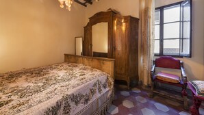 A bedroom with a bed, a wooden wardrobe, a chair, and a window with curtains. - Pinocchio by Mmega (Florence)