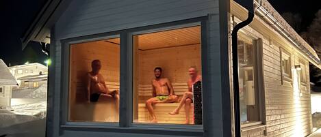Una cabaña de madera de un piso con techo inclinado, ventanas grandes y suelo cubierto de nieve.