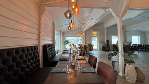 A restaurant with a long dining table, cushioned booths, and hanging pendant lights. - Senja Fjordcamp - Senja by Heart (Torsken)