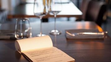 An open menu on a wooden table with glasses and a smartphone nearby.