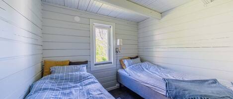 Una cabaña pequeña con dos camas, una ventana y una lámpara.