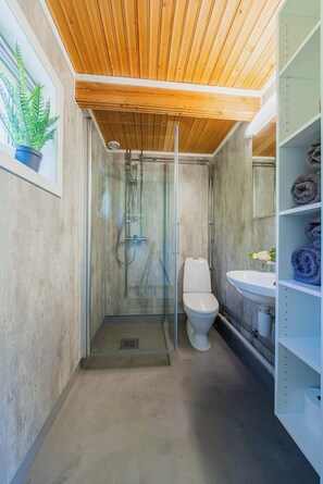 A compact bathroom with a glass shower enclosure, a toilet, and a built-in sink with a towel rack. - Senja Fjordcamp - Senja by Heart (Torsken)
