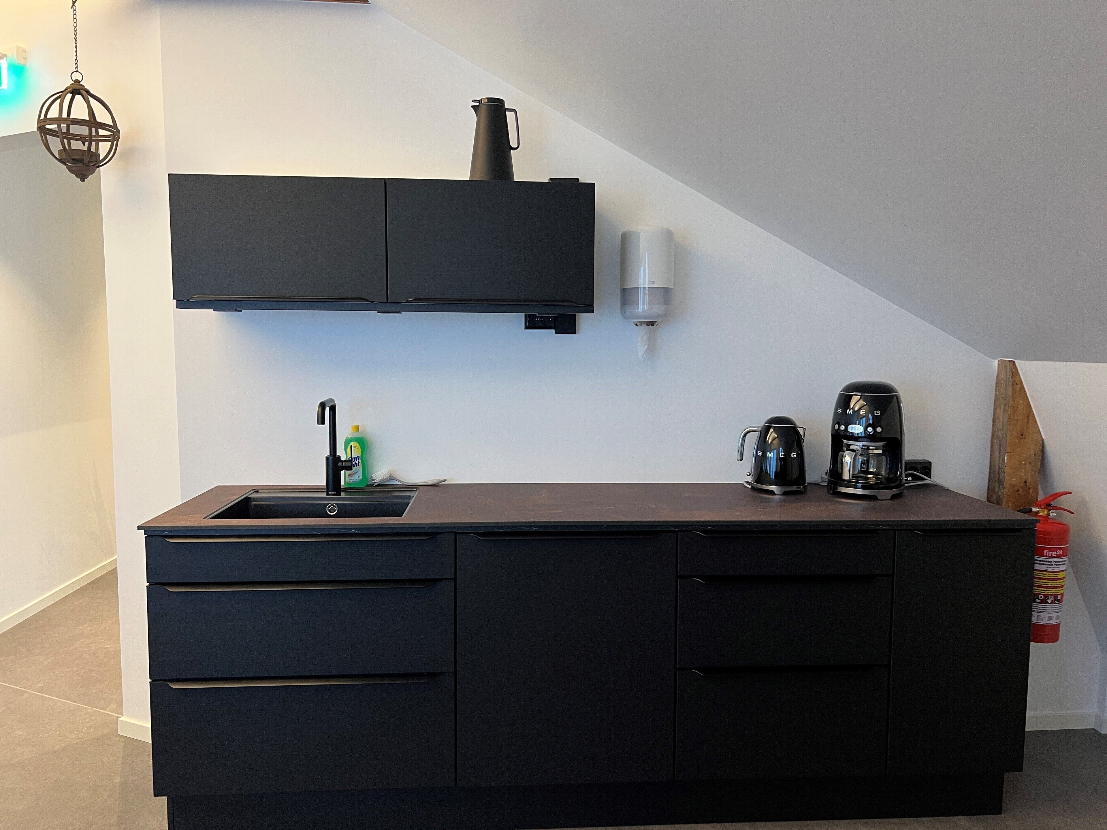 A modern kitchen with a built-in sink, black cabinets, a coffee maker, and a kettle.