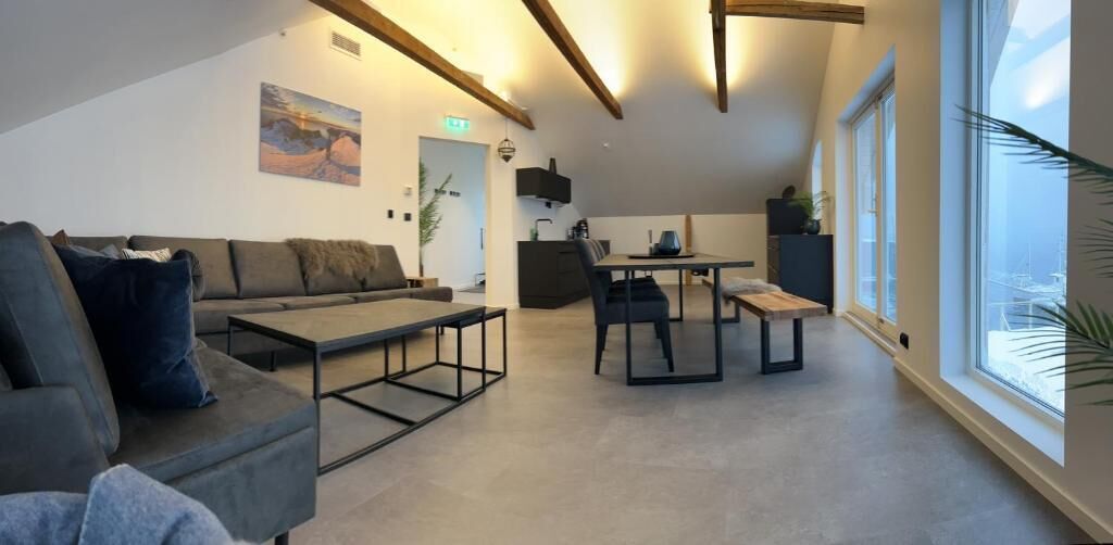 Ein großzügiger Wohnbereich mit Sofa, Couchtisch und Esstisch. Ein großes Fenster sorgt für Tageslicht und bietet einen Ausblick ins Freie.