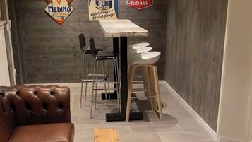 Una sala de estar moderna con un sofá de cuero marrón, un banco de madera, una mesa de comedor con sillas y una pared decorada con letreros antiguos.