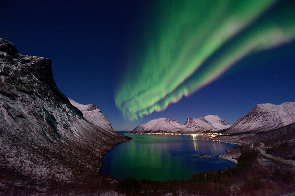 Paisaje nocturno con montañas nevadas, un lago tranquilo y las auroras boreales.