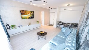 A modern living room with a light-colored sofa, a round coffee table, and a dining area with a table and chairs. - Celeste - One Bedroom Apartment - Next to Victoria Avenue and Cismigiu Park (Bucharest)