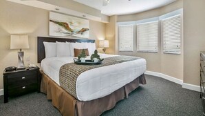 Habitación de hotel con una cama grande, un ventilador de techo, un cuadro en la pared y una ventana con persianas.