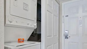 Un cuarto de lavandería con lavadora y secadora, una puerta y piso de baldosas.