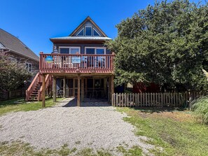 A two-story wooden house with a balcony, a gravel driveway, and a wooden fence. - SeaClusion I and SeaClusion II: Centrally located, perfect for biking or walking (Ocracoke)