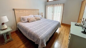 Ein Schlafzimmer mit einem Holzbett, einem Nachttisch mit Lampe, einem Fenster mit Vorhängen und Holzboden.