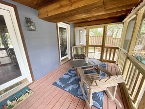 A covered porch with a wooden bench, a table with a vase, and a view of the backyard.