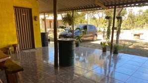 Ein überdachter Patio-Bereich mit Fliesenboden, einem schwarzen Fass, Topfpflanzen und einem geparkten Auto.