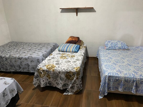 Une chambre avec deux lits simples, chacun recouvert d’une courtepointe à motifs, une petite étagère au-dessus des lits et un plancher en bois.