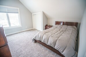 A bedroom with a sloped ceiling, a bed with a wooden headboard, a bedside table, and a window with blinds.