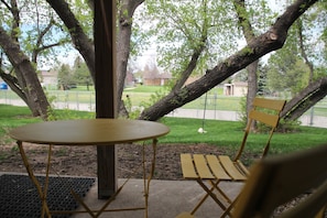 Relax in a serene outdoor setting with a round table and two chairs, shaded by a majestic tree branch.
