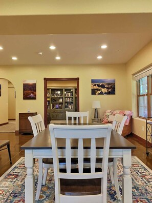 A dining area with a wooden table and chairs, a bookshelf, and a sofa. - Sturgis Neighborhood-Large Bedrooms-Patio-Views (Sturgis)