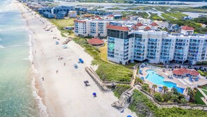 A beachfront hotel with multiple buildings, a swimming pool, and a beach with umbrellas. - 3BR Oceanfront Resort w/ Beach & Pool Access (North Topsail Beach)