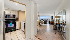 A modern kitchen with white cabinetry, a black oven, and a dining area with a wooden table and chairs. - 3BR Oceanfront Resort w/ Beach & Pool Access (North Topsail Beach)