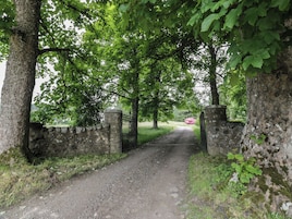A gravel path leading through a stone gate surrounded by trees.
