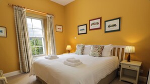 A neatly made bed with white linens and towels, a bedside table with a lamp, and three framed pictures on the wall. - Fordie South Cottage (Crieff)