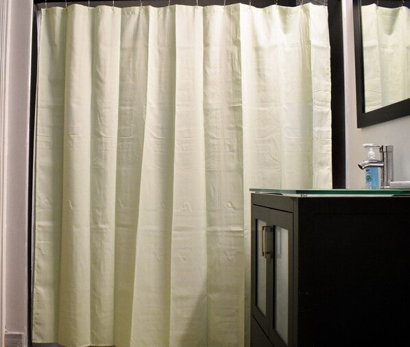 A bathroom with a white shower curtain, a mirror, and a sink with a soap dispenser.
