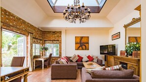 Un salon spacieux avec un haut plafond, un lustre, une cheminée et un téléviseur.