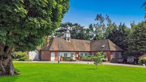 Une maison à deux étages, construite en briques, avec une porte de garage blanche, entourée d’une pelouse bien entretenue et d’arbres.