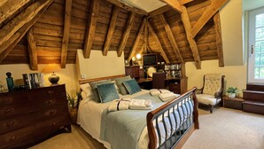 Une chambre avec un plafond en bois, un lit recouvert d’une couverture bleue, une commode, un bureau avec un ordinateur et une chaise.